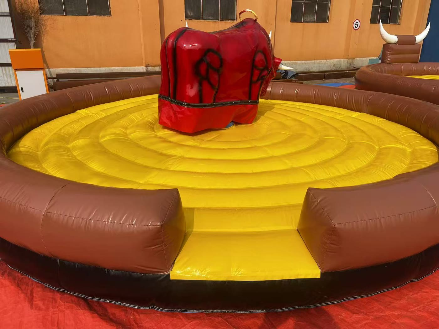 Red mechanical bull inside a yellow inflatable ring in the factory yard