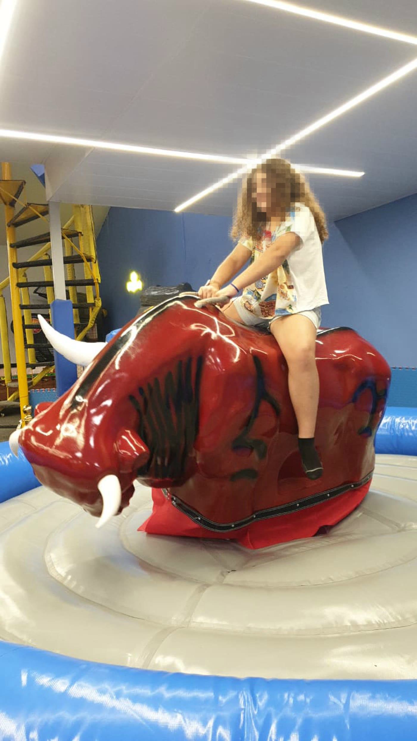 Girl riding a red mechanical bull at an indoor family entertainment centre